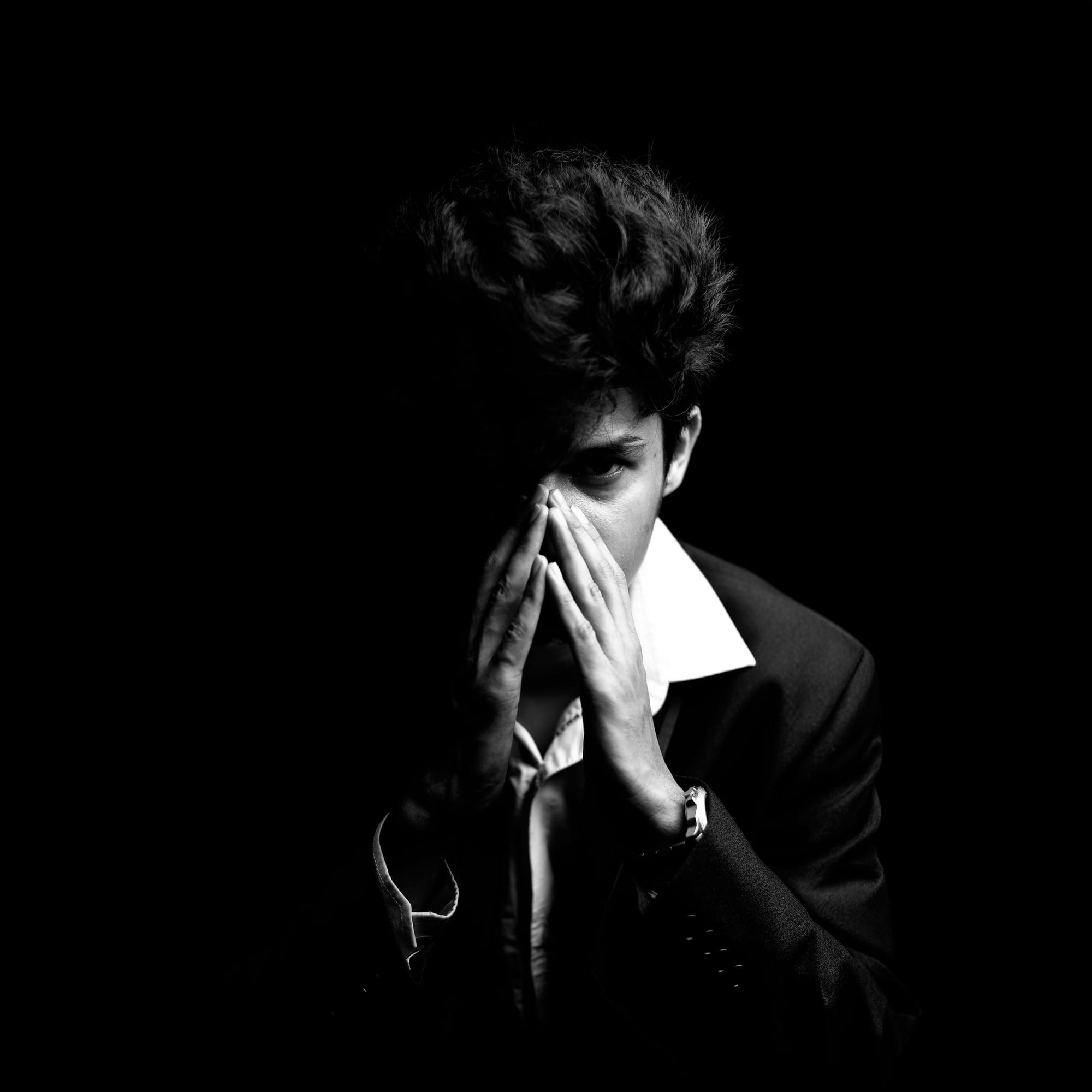 Ein junger Mann hält die gefalteten Hände vor das Gesicht, umgeben von Dunkelheit