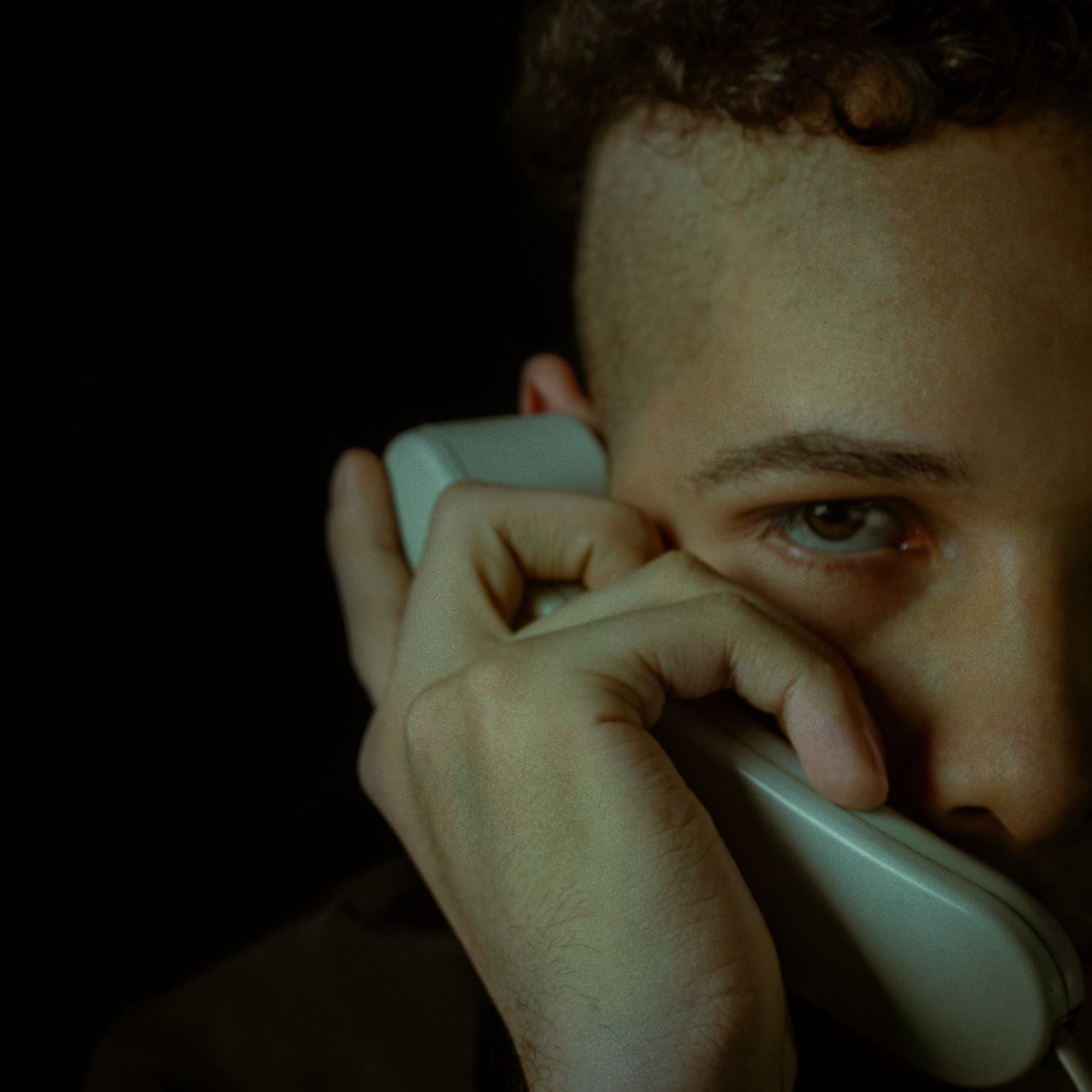 Ein junger Mann hält einen alten Telefonhörer ans Ohr und blickt unsicher zur Seite